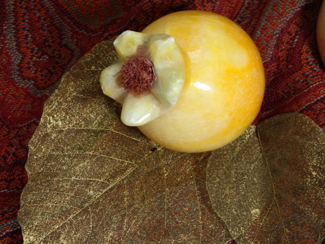 Yellow ceramic fruit on gold leaves and red fabric